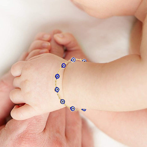 A close-up of a baby's hand adorned with the Blue Evil Eye Charm Bracelet for Protection Good Luck Turkish Nazar, delicately holding an adult's finger.
